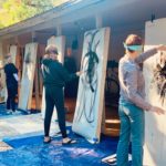 Multiple people at individual large canvases painting with black ink on white paper. They are blindfolded and participating in one of Dr. Sobo's outdoor gestural art therapy workshops.