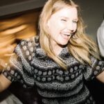 Picture of a white woman with shoulder length light brown hair dancing happily.